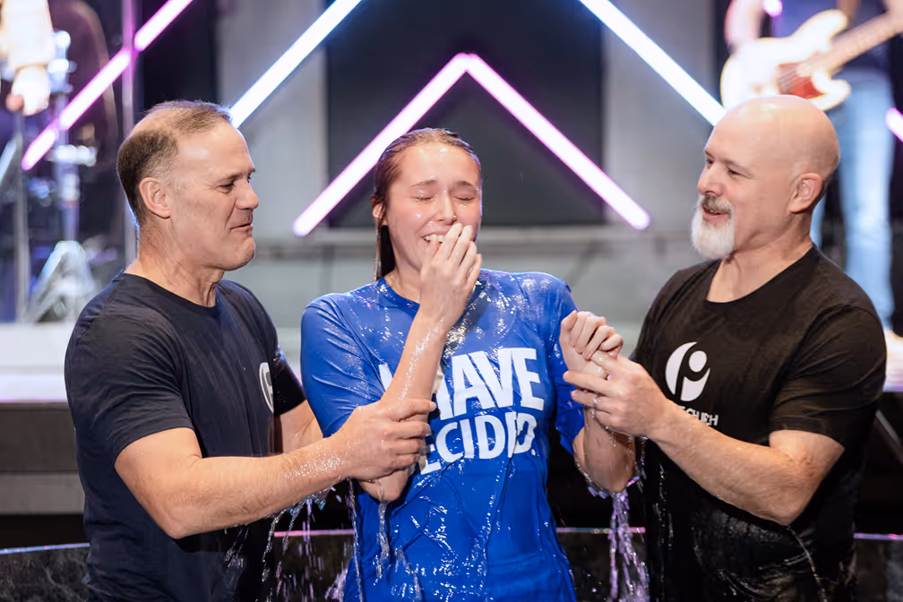 A woman baptizing a young girl in a baptismal pool, with water splashing around them.