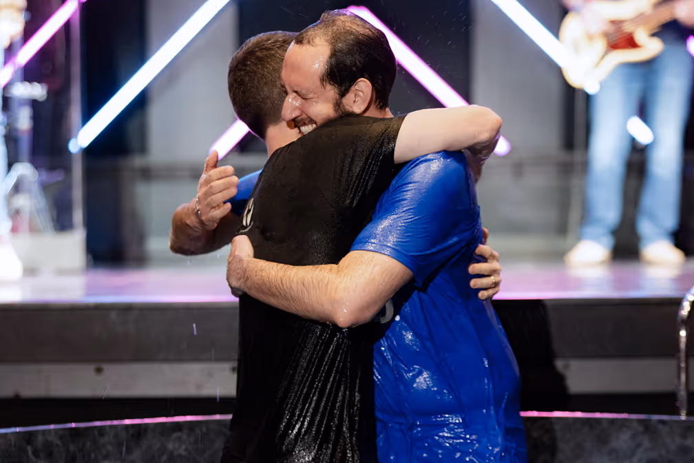 A woman baptizing a young girl in a baptismal pool, with water splashing around them.