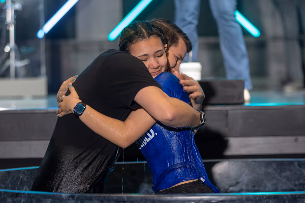 A woman baptizing a young girl in a baptismal pool, with water splashing around them.