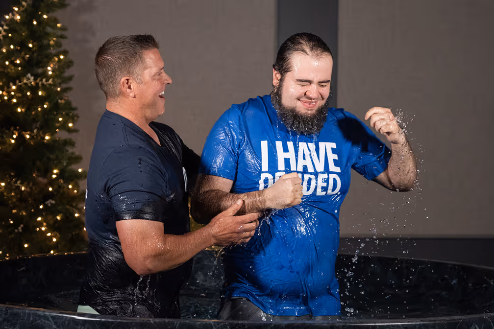 A woman baptizing a young girl in a baptismal pool, with water splashing around them.