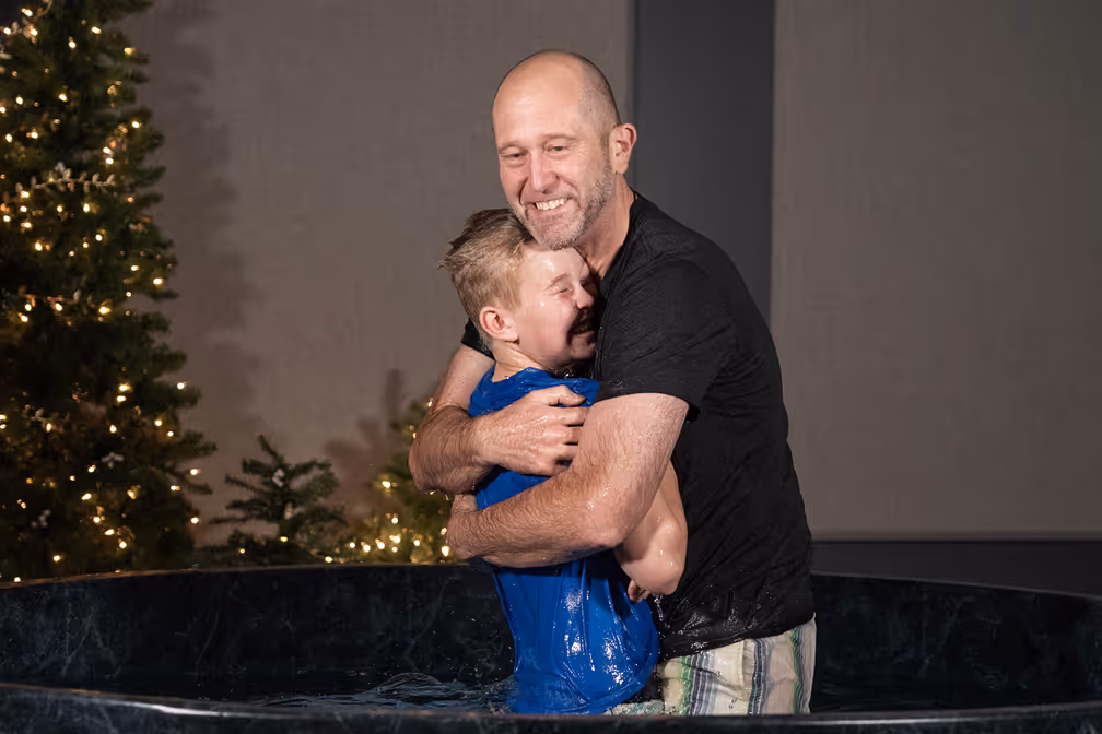 A woman baptizing a young girl in a baptismal pool, with water splashing around them.
