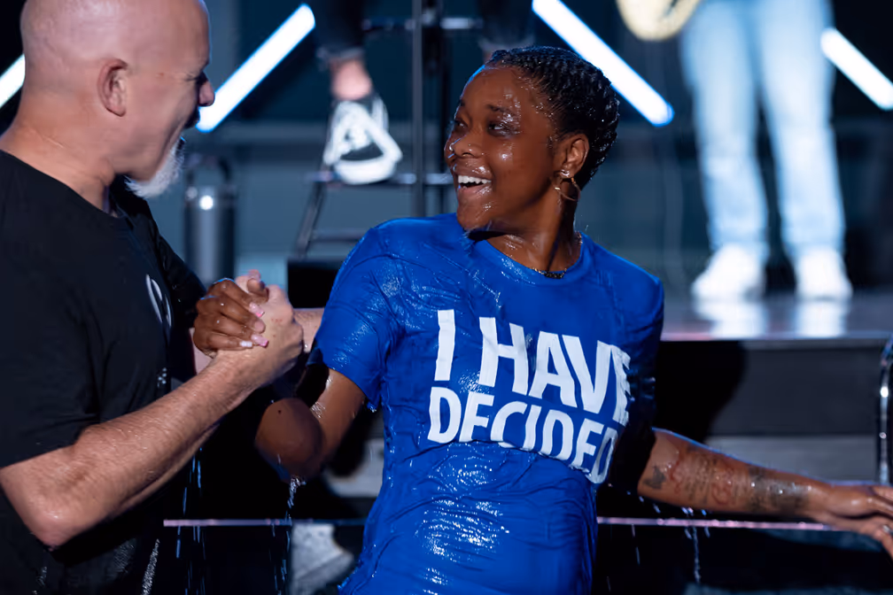 A woman baptizing a young girl in a baptismal pool, with water splashing around them.