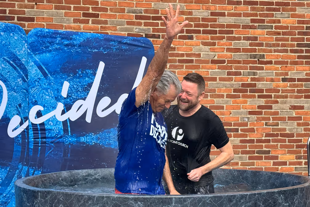 A woman baptizing a young girl in a baptismal pool, with water splashing around them.