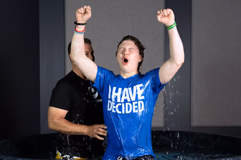 A woman baptizing a young girl in a baptismal pool, with water splashing around them.