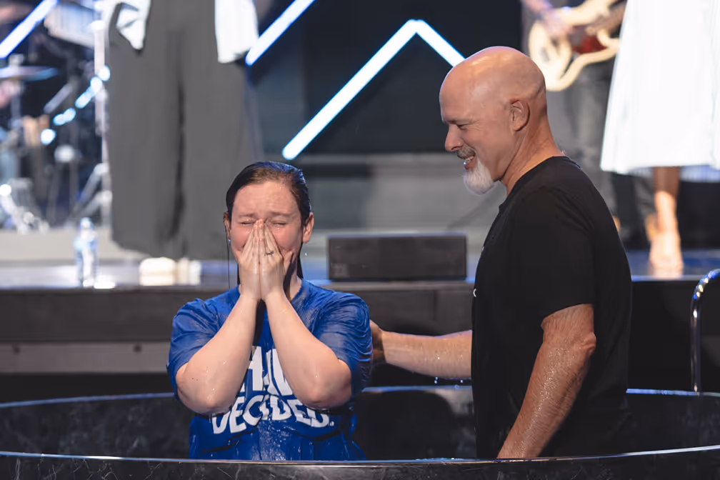 A woman baptizing a young girl in a baptismal pool, with water splashing around them.