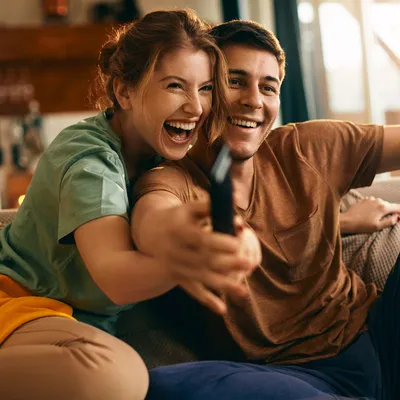 Um casal jovem se diverte assistindo Paramount na sala de estar, curtindo momentos de descontração enquanto desfrutam de um bom filme juntos.