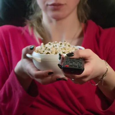 Com uma tigela de pipoca em mãos e o controle remoto ao seu alcance, uma jovem mulher está pronta para relaxar e assistir ao Globoplay.