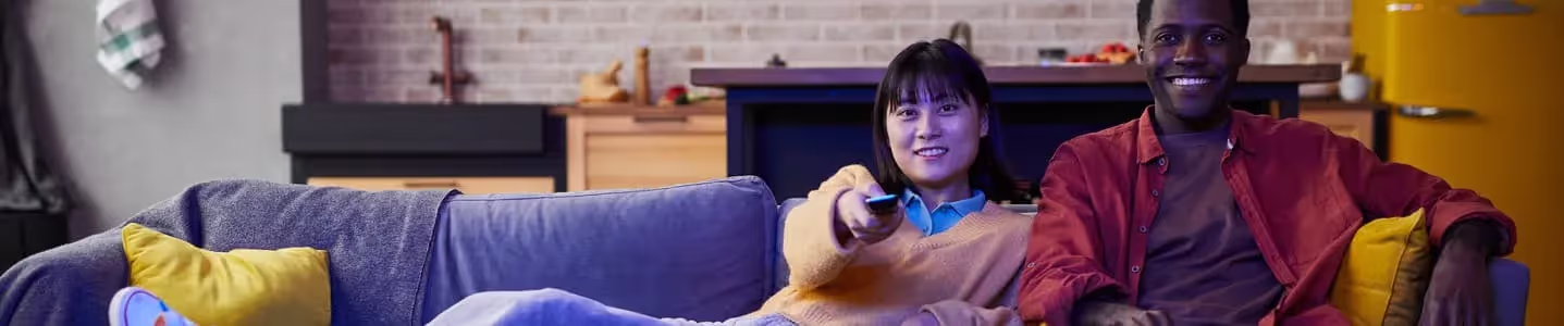 Em um sofá azul, o casal feliz aproveita a TV juntos: a mulher deitada e o homem sentado, compartilhando momentos de alegria e descontração.