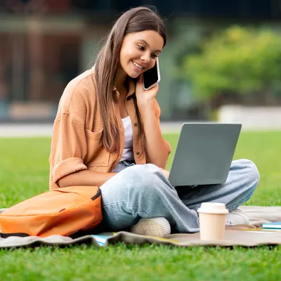 Mulher jovem aproveita a tranquilidade do campo para usufruir dos serviços do Combo Oi em seu celular e notebook.