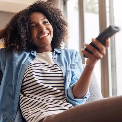 Com um sorriso radiante, uma jovem mulher demonstra felicidade ao baixar um novo aplicativo na TV, ansiosa para aproveitar as diversas possibilidades de entretenimento e funcionalidades oferecidas.