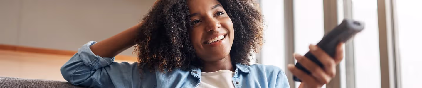 Com alegria estampada no rosto, uma jovem mulher se encontra feliz ao baixar um aplicativo na TV, preparando-se para explorar novas opções de entretenimento e funcionalidades diretamente na tela grande.