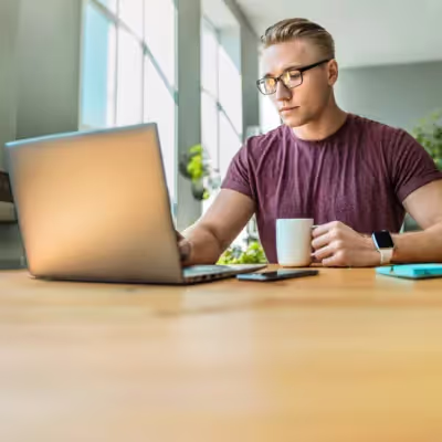 Homem trabalhando sentado no escritório de casa com uma xícara de café e caderno.