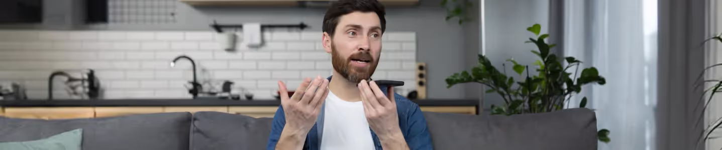 Homem conversando com a Siri no celular em casa.