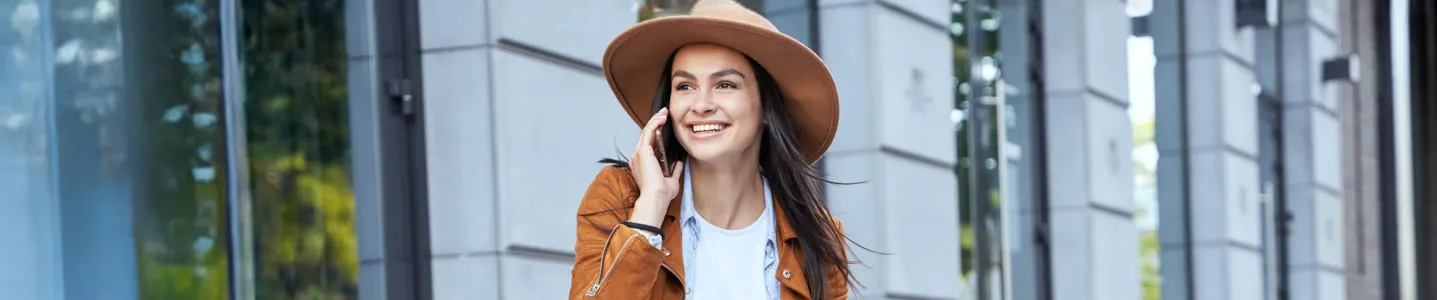 Mulher de chapéu sentada na escada falando ao celular.