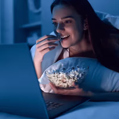 Cheia de animação, uma mulher empolga-se para assistir ao Globoplay, degustando pipoca com expectativa enquanto se prepara para uma sessão de entretenimento.