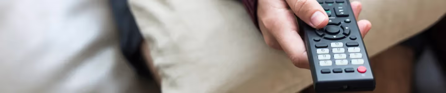 Com o controle remoto em mãos, um rapaz navega com habilidade para selecionar a programação desejada no Globoplay, personalizando sua experiência de visualização de acordo com suas preferências.