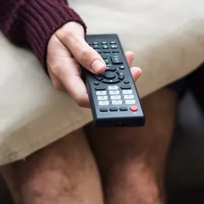 Usando o controle remoto com destreza, um rapaz navega pelas opções do Globoplay, escolhendo a programação que mais lhe agrada e personalizando sua experiência de entretenimento.