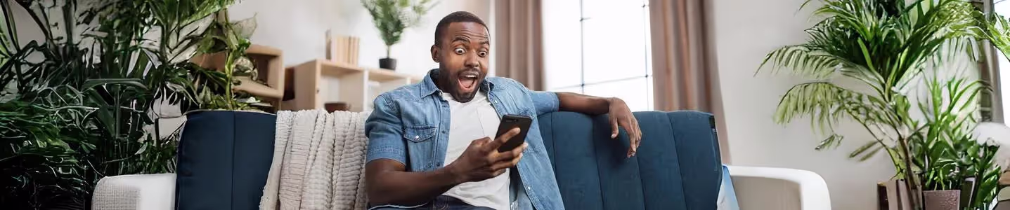 Homem em casa, lendo boas notícias no celular.