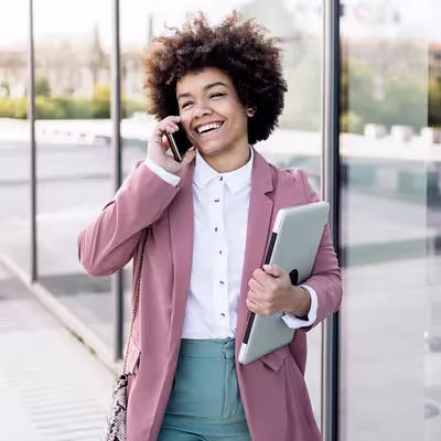 A jovem mulher está animada enquanto realiza uma ligação alegremente em seu smartphone, demonstrando uma comunicação leve e descontraída.