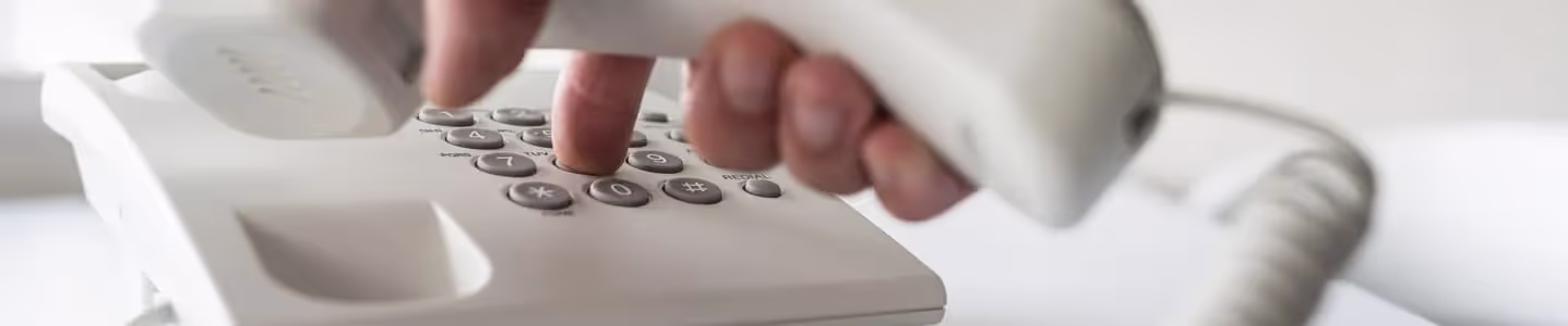 Uma mão masculina segura firmemente o telefone de fio enquanto digita com destreza um número com a mesma mão, mostrando habilidade multitarefa.