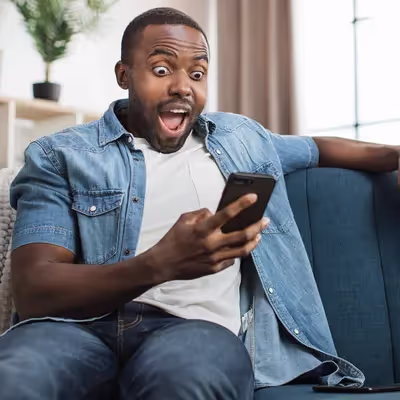 Homem feliz lendo notícias positivas em seu celular, em casa.