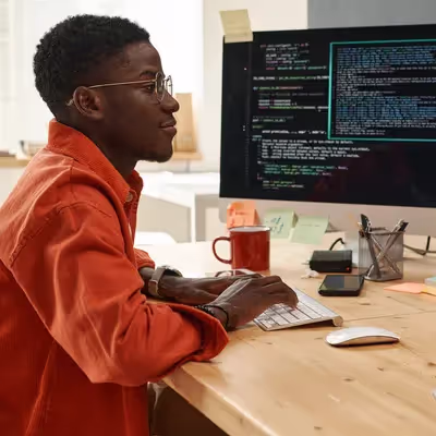 Um engenheiro de TI jovem e determinado, usando uma camiseta laranja inteligente, analisa dados codificados com seriedade, destacando sua expertise em lidar com informações digitais complexas.