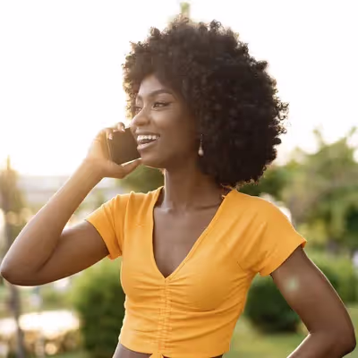 Com um sorriso no rosto, uma jovem mulher aproveita seu celular para desfrutar dos benefícios do plano Oi Alegria, usufruindo de diversas vantagens oferecidas pela operadora.