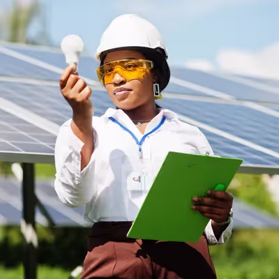 Diante de painéis solares, uma representante da Oi segura uma lâmpada, simbolizando o compromisso da empresa com a energia limpa e renovável