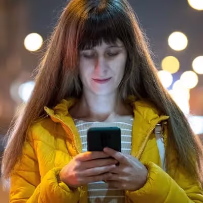 Jovem com jaqueta amarela navega no celular, sob a luz suave da tarde.