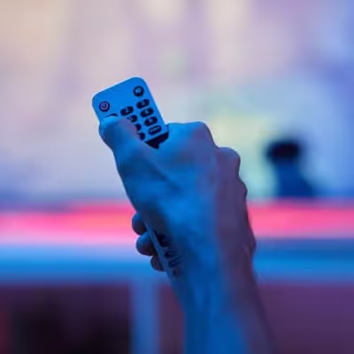 Em frente à TV, uma mão masculina maneja o controle remoto com domínio.
