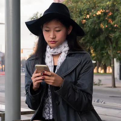 Sob a espera paciente no ponto de ônibus, uma jovem mulher se acomoda, entregando-se ao universo virtual em seu celular, enquanto aguarda o transporte que a levará ao próximo destino.