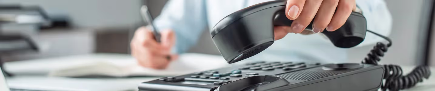 Mãos femininas pegam o telefone para fazer uma ligação na empresa que utiliza um sistema de PABX, destacando a comunicação eficiente e organizada no ambiente de trabalho.