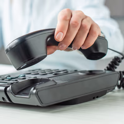 Uma mulher pega o telefone para fazer uma ligação na empresa que utiliza um sistema de PABX, demonstrando a praticidade e a familiaridade com a tecnologia de comunicação interna da organização.