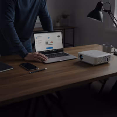 Homem em pé, utilizando notebook e projetor em mesa