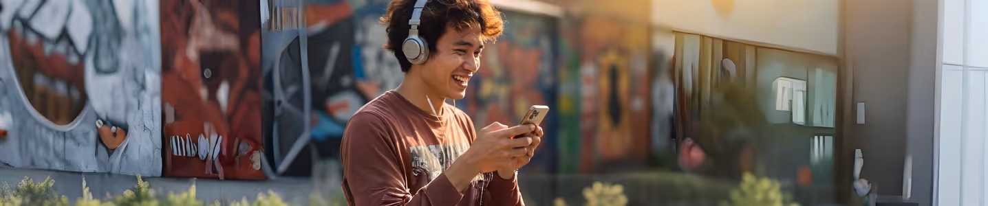 Jovem ouvindo música com fones e celular na rua grafitada