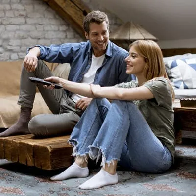 Num clima acolhedor, o casal se acomoda para uma sessão de filme, folheando as opções, em busca do título perfeito para desfrutar juntos, criando memórias agradáveis.