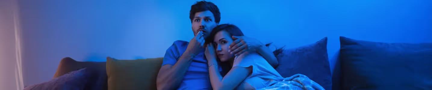 Casal assistindo filme de suspense na TV juntos.