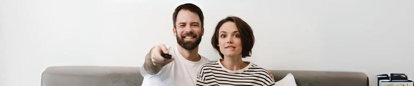 Jovem casal sorri enquanto assiste TV juntos.