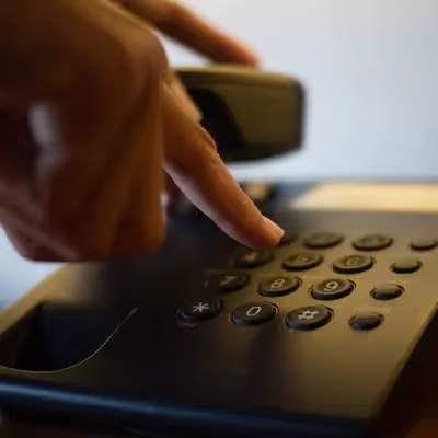 Mão digitando números no teclado do telefone com fio, realizando uma ligação.