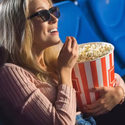 Jovem mulher loira sorridente aproveitando a pipoca enquanto assiste algo empolgante.