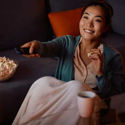 A jovem mulher aproveita sua TV 4K para uma experiência de cinema envolvente, mergulhando em imagens nítidas e cores vibrantes que transformam sua sala em uma sala de cinema pessoal.