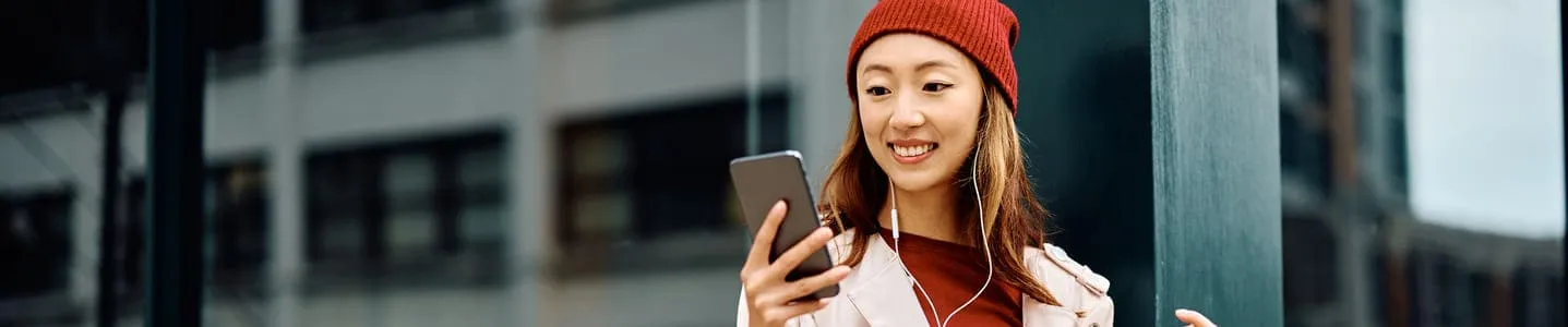 Jovem mulher feliz, segurando sacolas de compras, sorri enquanto olha para o celular, talvez compartilhando suas últimas descobertas de compras ou recebendo uma mensagem animada.