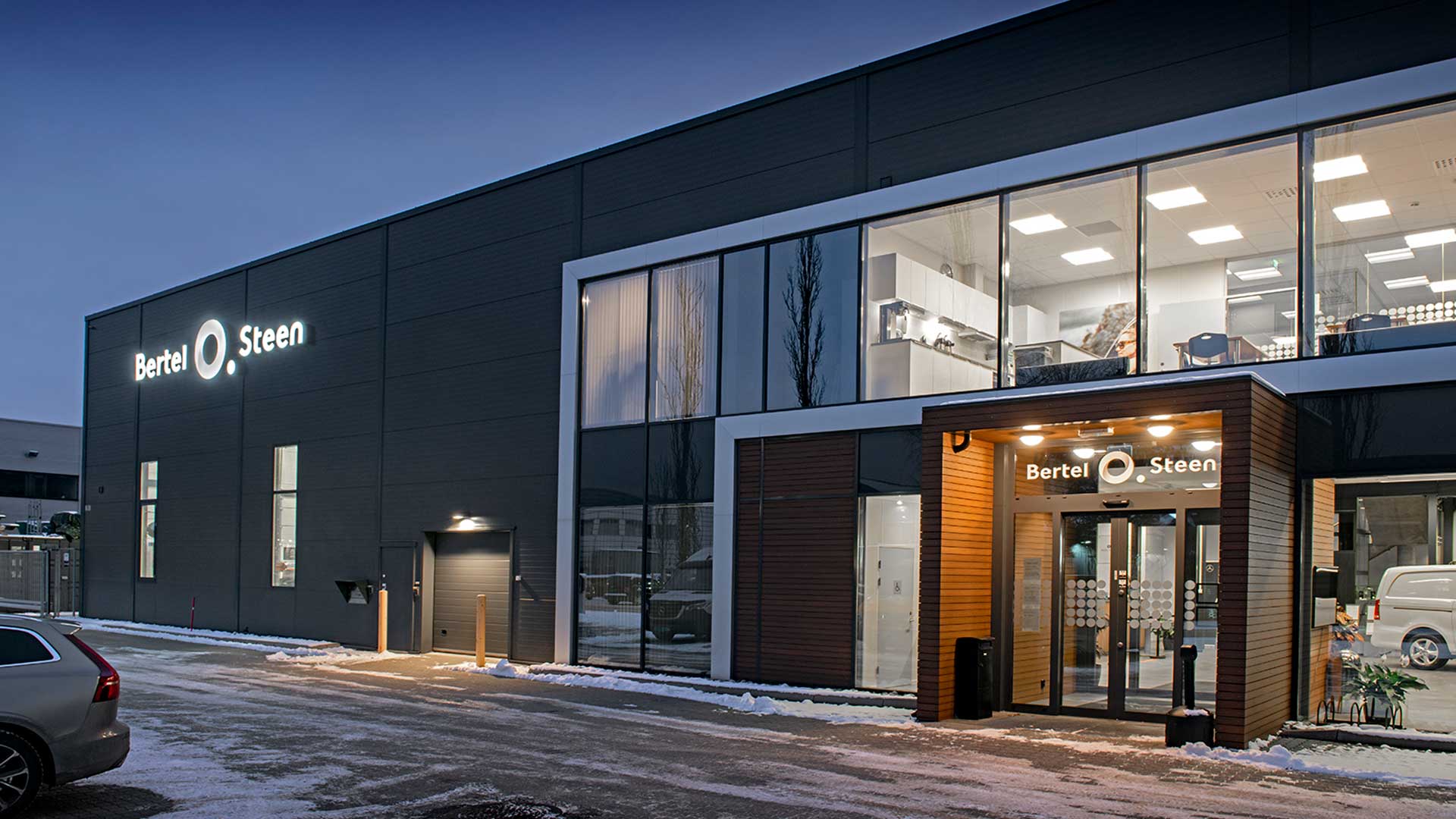 Fasade av Bertel O. Steen-bygg med opplyst inngangsparti om kvelden og snø på bakken.
