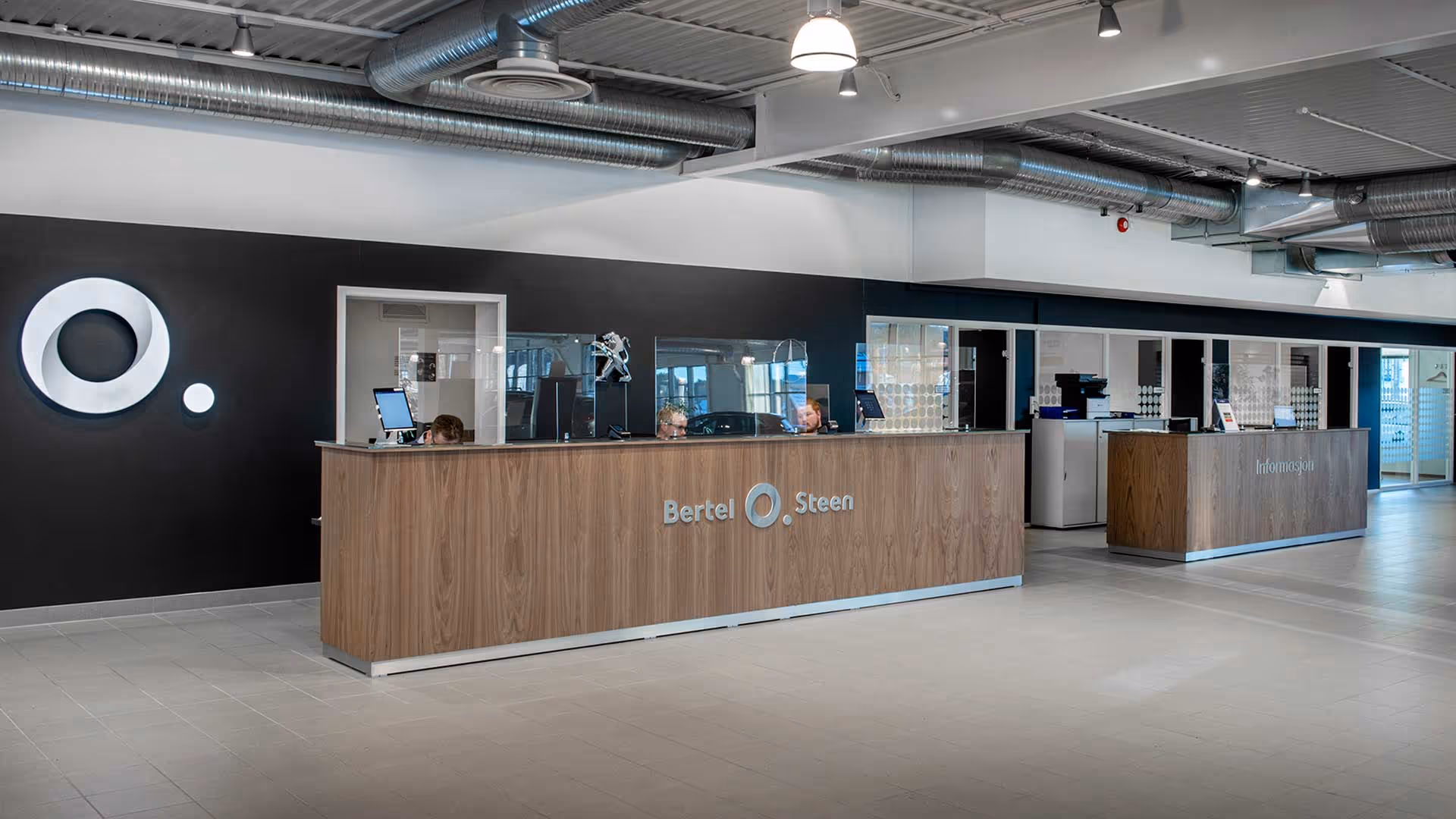 Resepsjonsområde med to tre- og glassdisker merket Bertel O. Steen og Informasjon, med ansatte bak diskene.