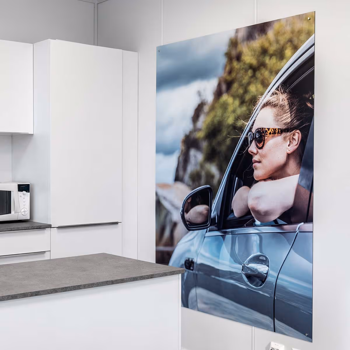 Kjøkkeninteriør med hvite skap og en stor bildevegg av en kvinne med solbriller som ser ut av bilvinduet.