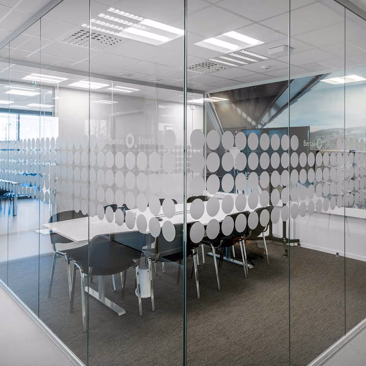 Moderne møterom med glassvegger dekorert med hvite sirkler og et hvitt bord omgitt av svarte stoler.