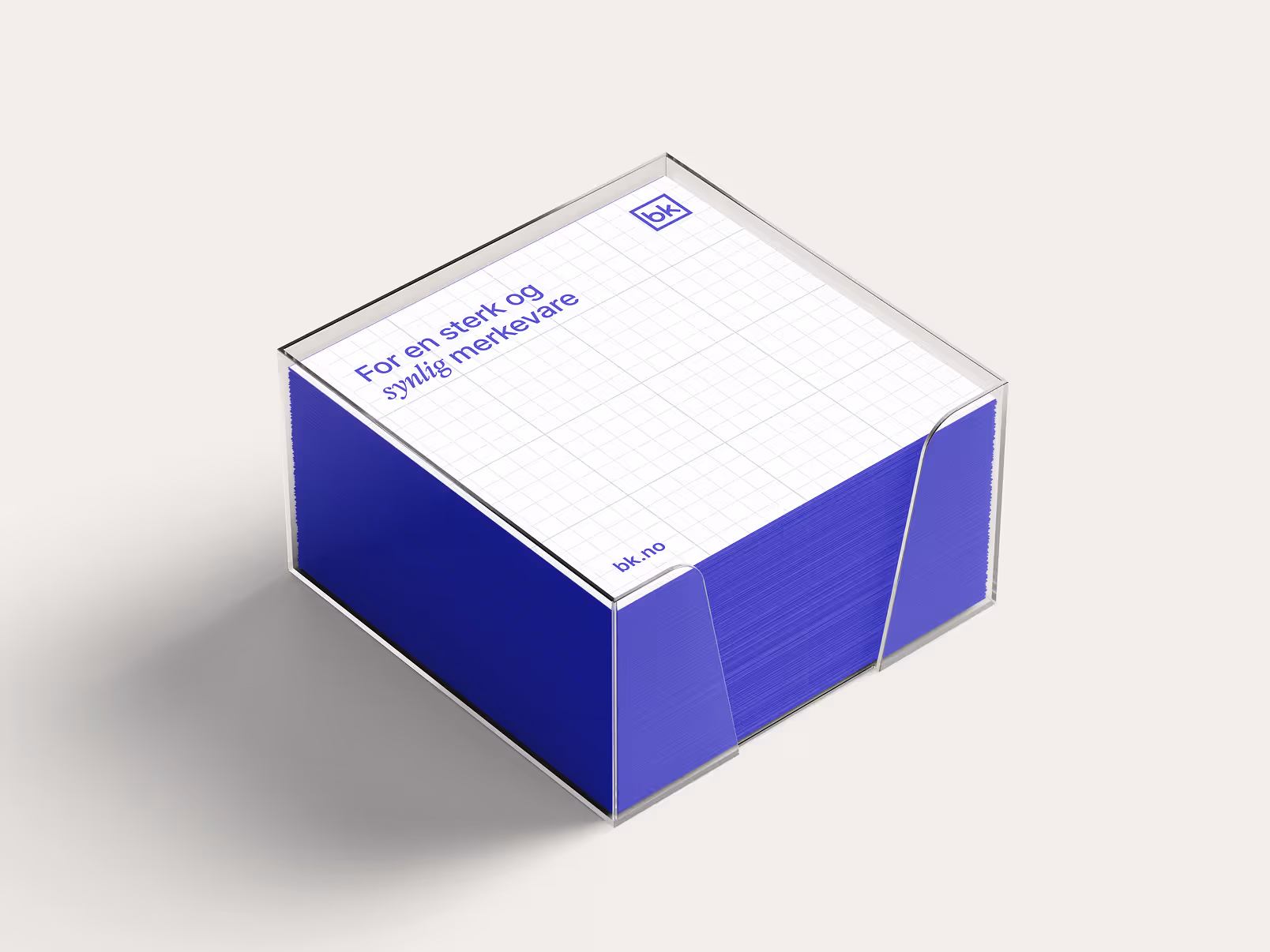 En gjennomsiktig eske med en blokk notater som har blå sider og et rutenettmønster øverst med teksten 'For en sterk og synlig merkevare'.