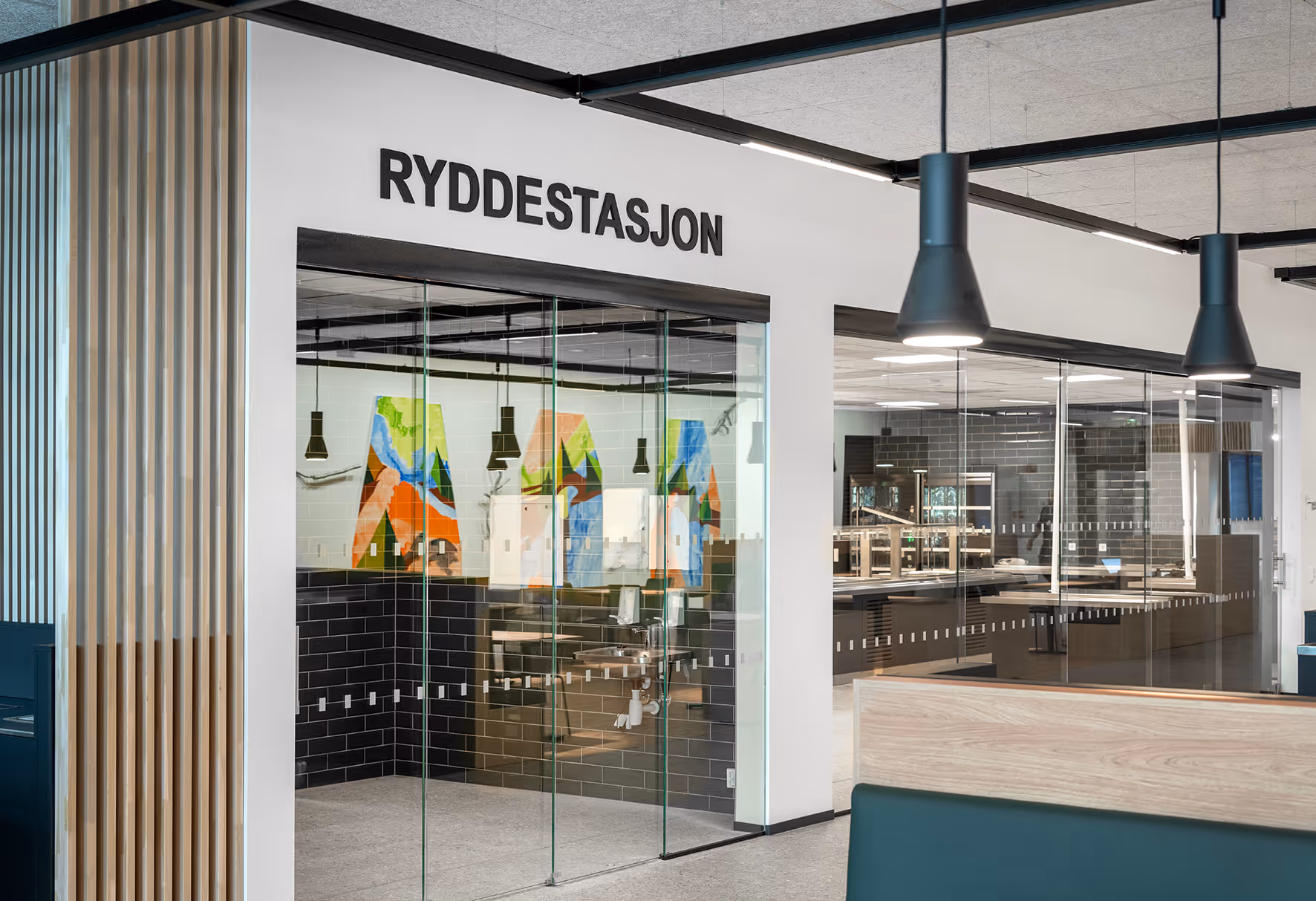 Moderne rom med glassvegger merket 'Ryddestasjon' og fargerik veggkunst i bakgrunnen.