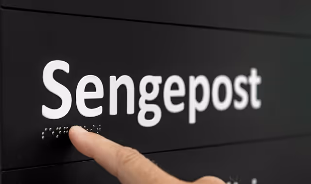 En finger som leser punktskrift under teksten 'Sengepost' på et svart skilt.