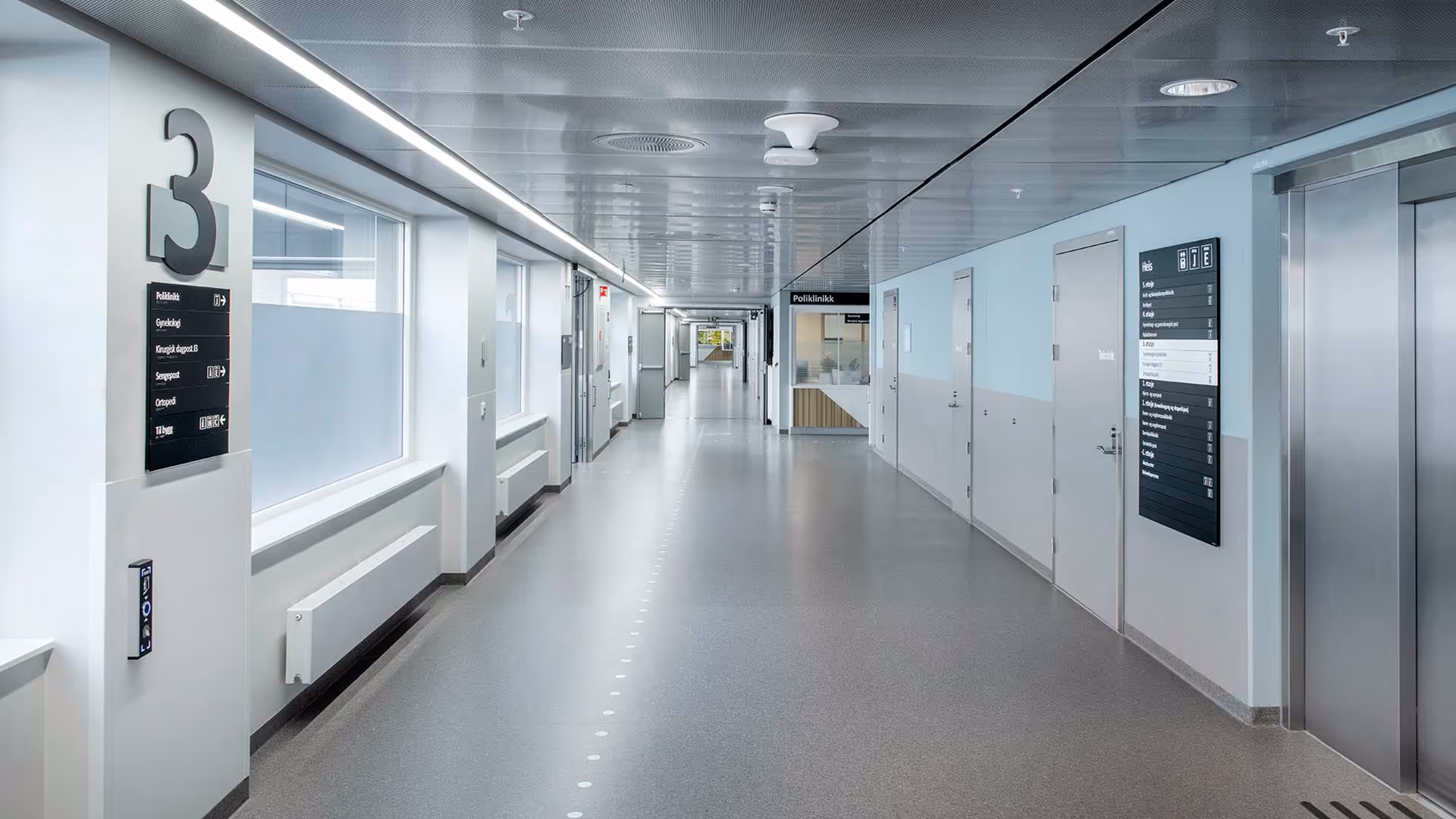 Lys og ren sykehusgang med heis, dører og skilting for poliklinikk og medisinske avdelinger.
